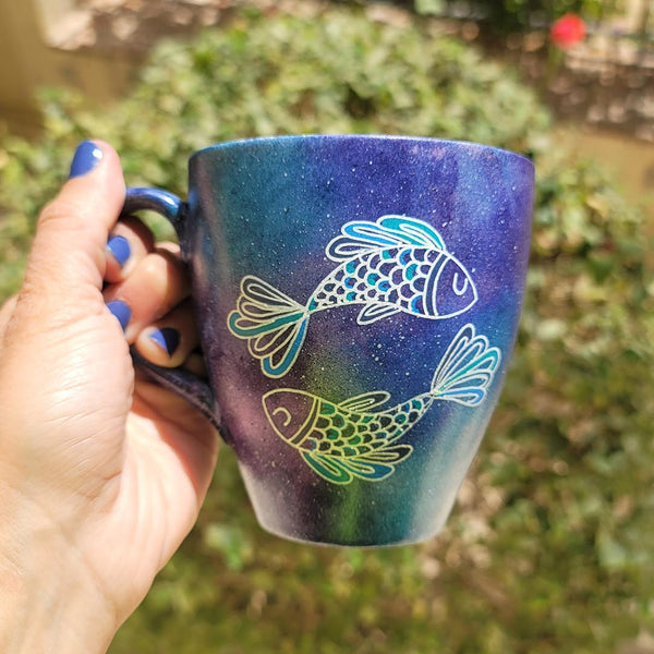 A Handpainted blue galaxy mug with a Pisces design on it