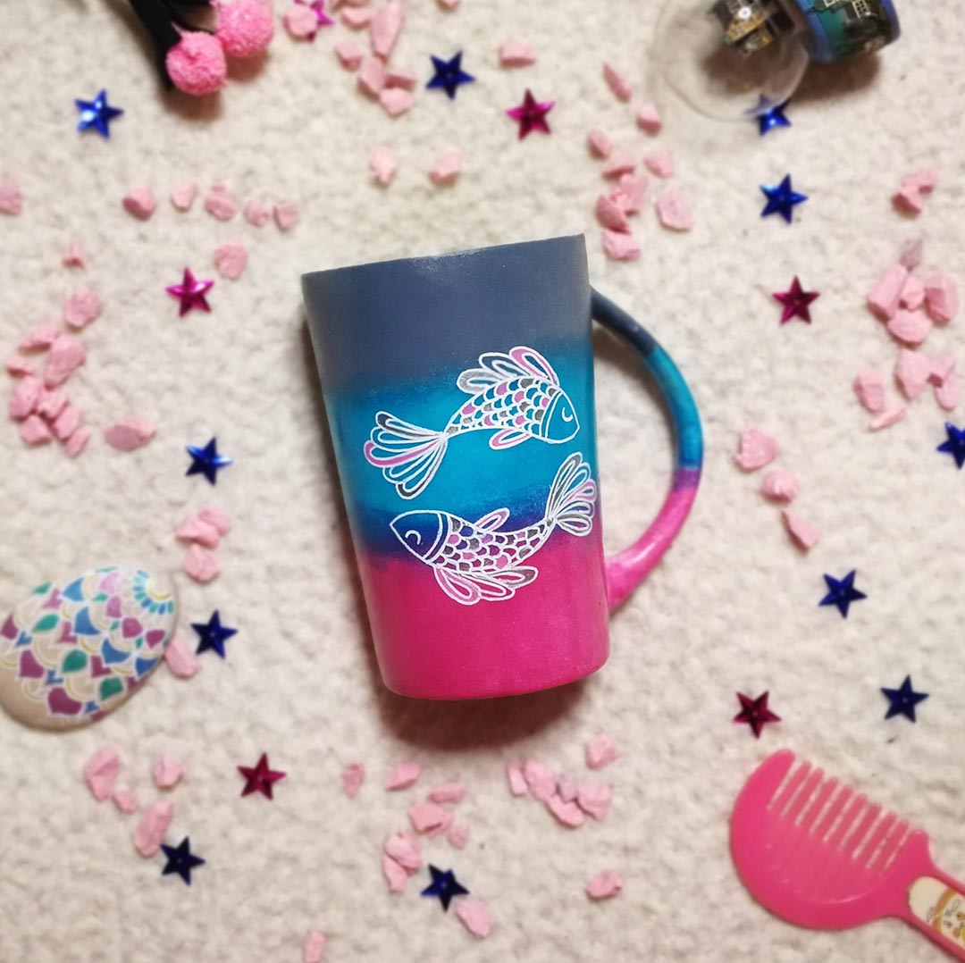 A Handpainted degradeh (grey-blue-pink) mug with a Pisces design on it