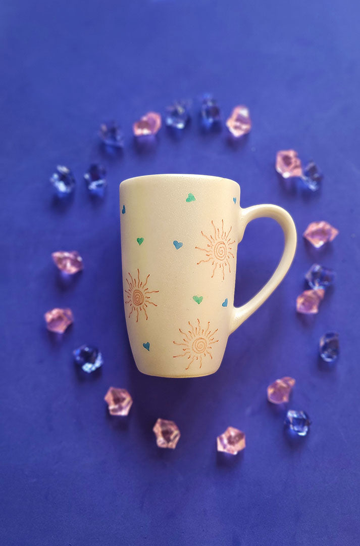 An Ivory Hand painted mug with small doodle suns and small hearts scattered all over the mug