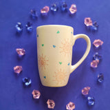 An Ivory Hand painted mug with small doodle suns and small hearts scattered all over the mug