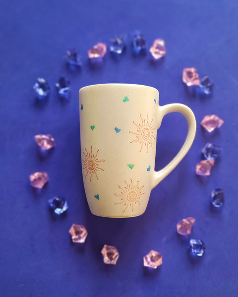 An Ivory Hand painted mug with small doodle suns and small hearts scattered all over the mug