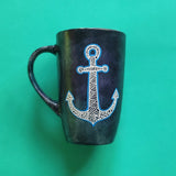 A Black sky hand painted mug with an anchor painted on it in patterns and outlined with blue