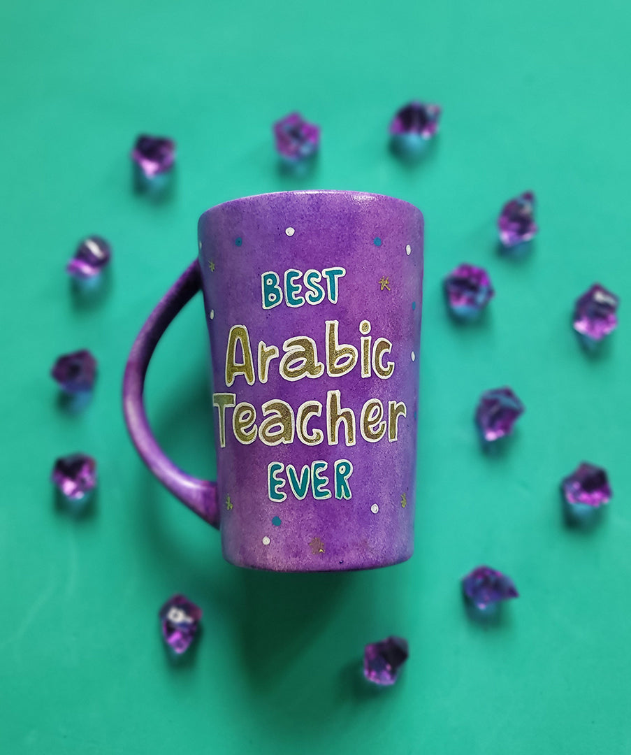 A Purple Hand painted mug with the words " best Arabic teacher Ever" with turquoise gold and white dots scattered all over