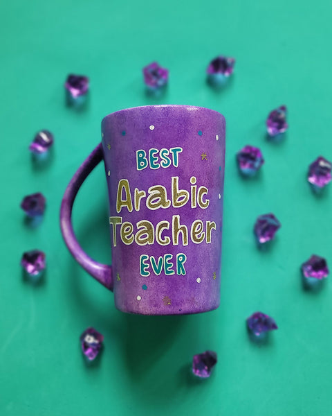 A Purple Hand painted mug with the words " best Arabic teacher Ever" with turquoise gold and white dots scattered all over