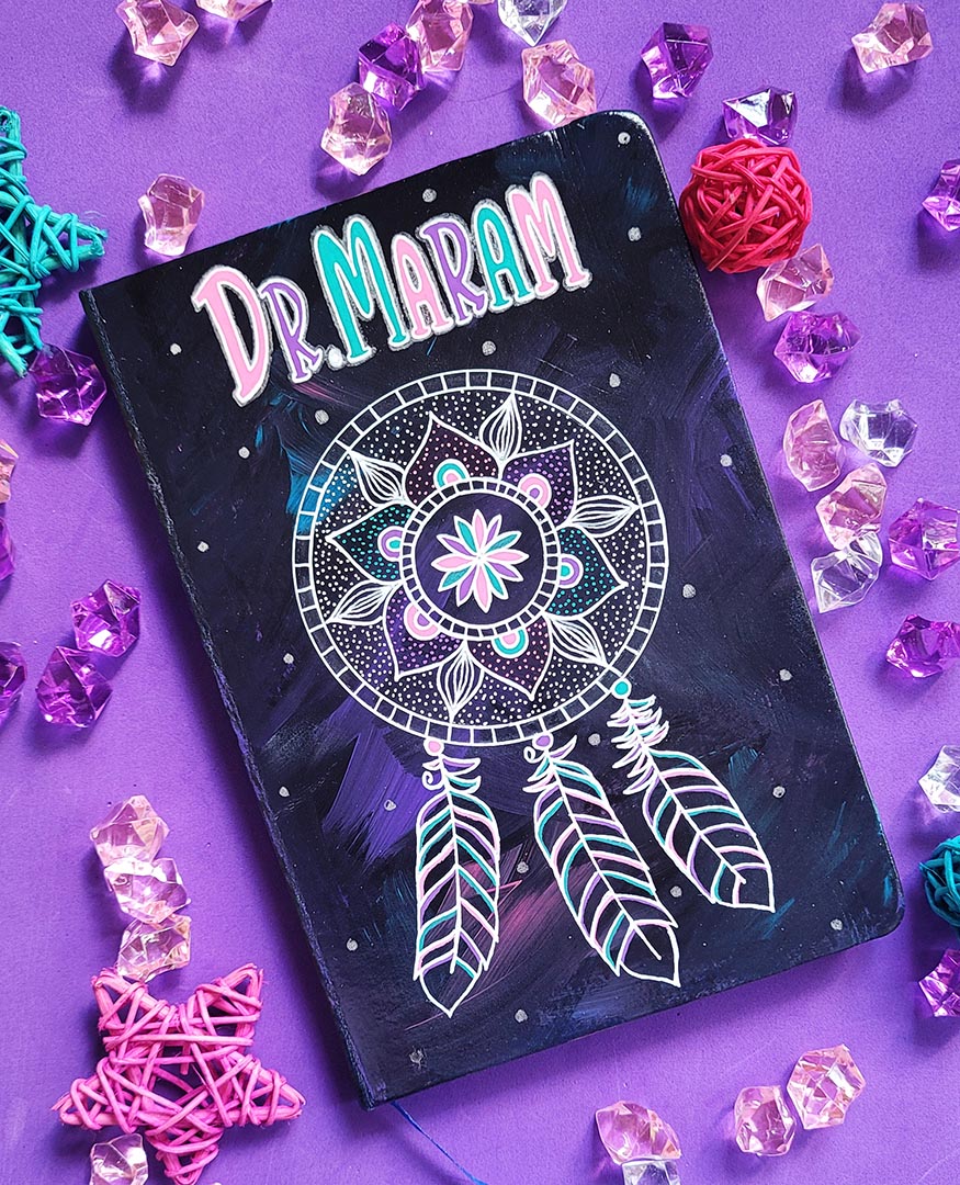 A Dark Sky hand painted notebook with a mandala drawn in white and the name "Dr.Maram" written in the top center