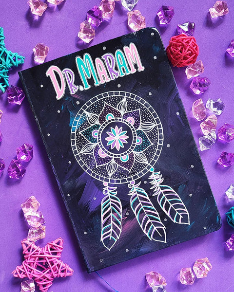 A Dark Sky hand painted notebook with a mandala drawn in white and the name "Dr.Maram" written in the top center