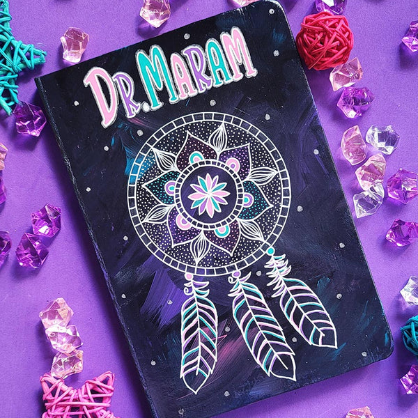 A Dark Sky hand painted notebook with a mandala drawn in white and the name "Dr.Maram" written in the top center