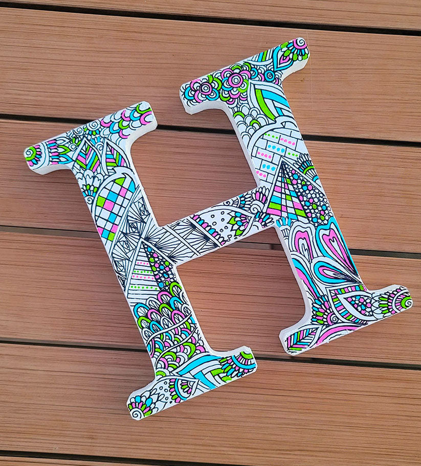 A white letter H with doodles in black and colored in with pink, lime green and light blue