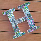 A white letter H with doodles in black and colored in with pink, lime green and light blue