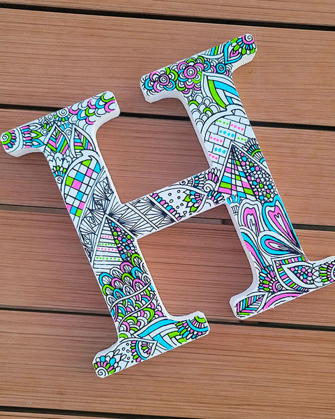 A white letter H with doodles in black and colored in with pink, lime green and light blue