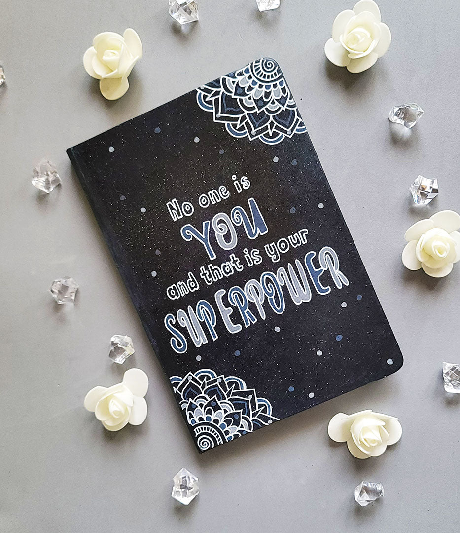 A Black Galaxy Hand painted notebook with 2 small mandala drawn in white in the opposite corners and the quote written in the center "no one is You and that is your Superpower"