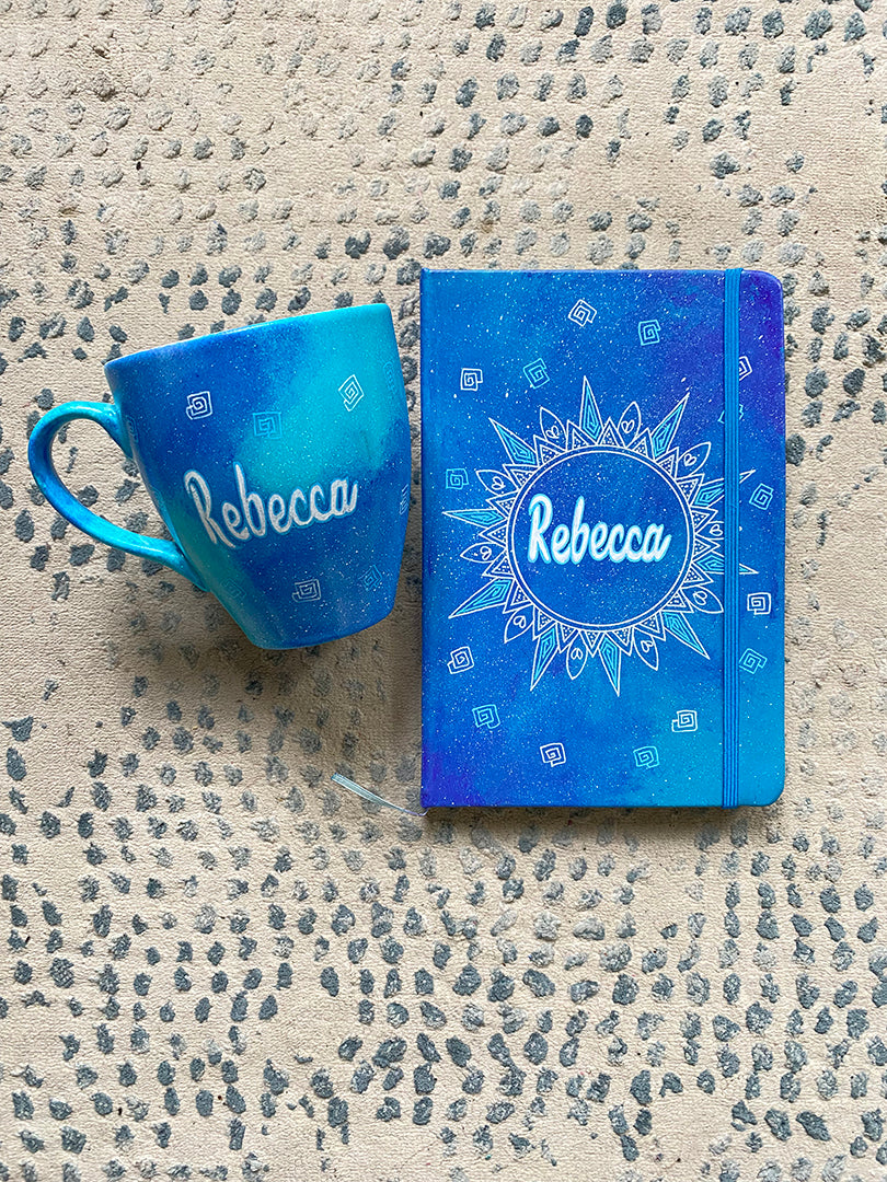 A Gift set of mug and notebook hand painted in blue galaxy. the mug has the name rebecca and the notebook has a mandala with the name rebecca in the center