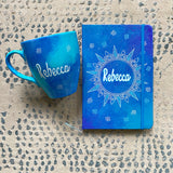 A Gift set of mug and notebook hand painted in blue galaxy. the mug has the name rebecca and the notebook has a mandala with the name rebecca in the center