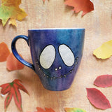 A bluish galaxy hand painted mug with a smiley scary face on it