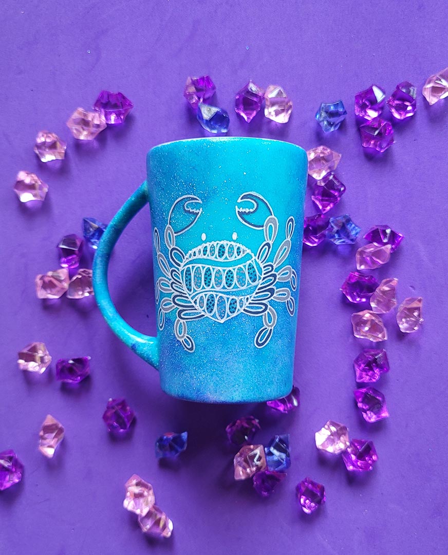 A hand-painted blue galaxy mug with cancer sign drawn on it