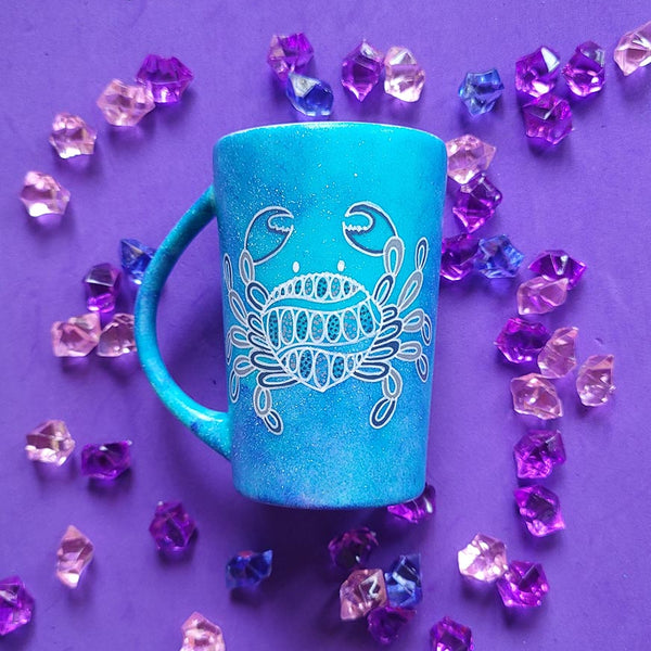 A hand-painted blue galaxy mug with cancer sign drawn on it