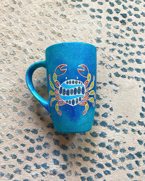 A hand-painted blue galaxy mug with cancer sign drawn on it