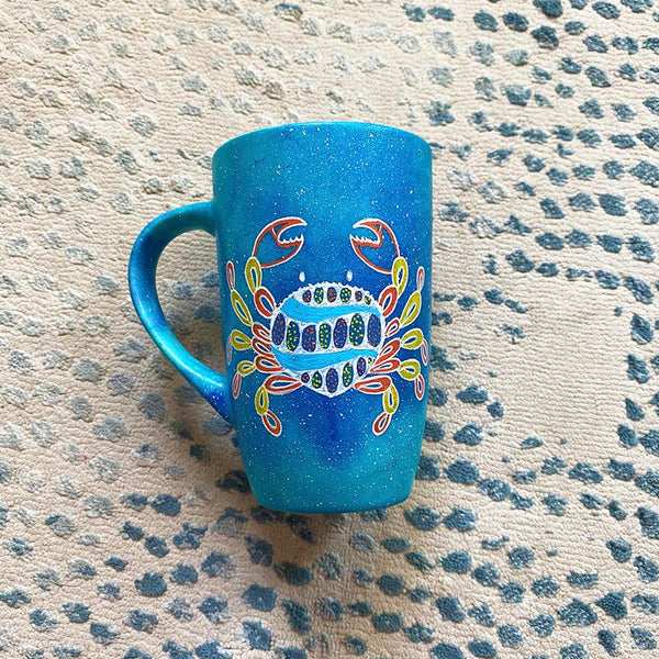 A hand-painted blue galaxy mug with cancer sign drawn on it