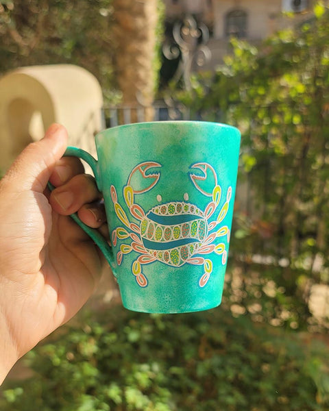 A hand-painted green  mug with cancer sign drawn on it