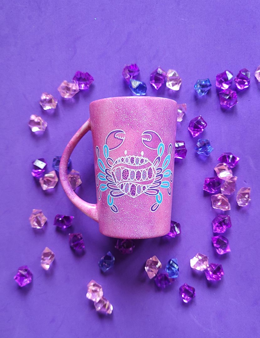 A hand-painted pink galaxy mug with cancer sign drawn on it