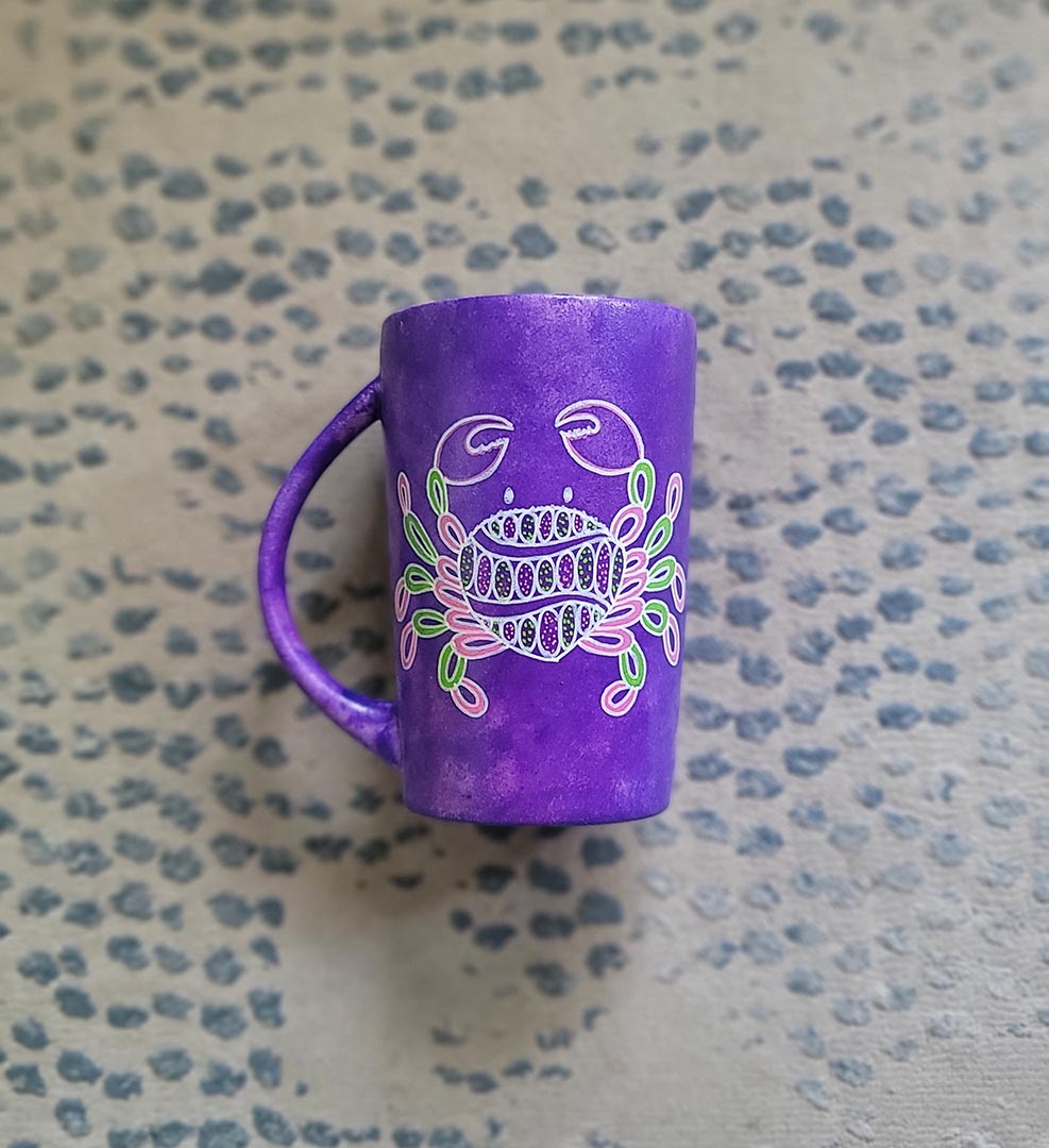 A hand-painted purple mug with cancer sign drawn on it