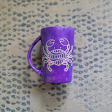 A hand-painted purple mug with cancer sign drawn on it