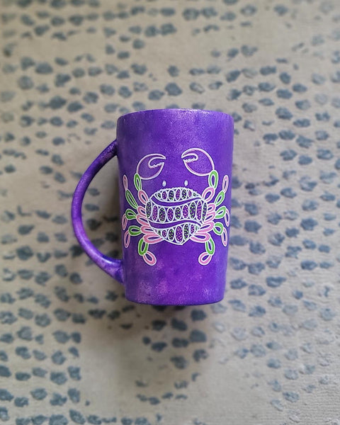 A hand-painted purple mug with cancer sign drawn on it