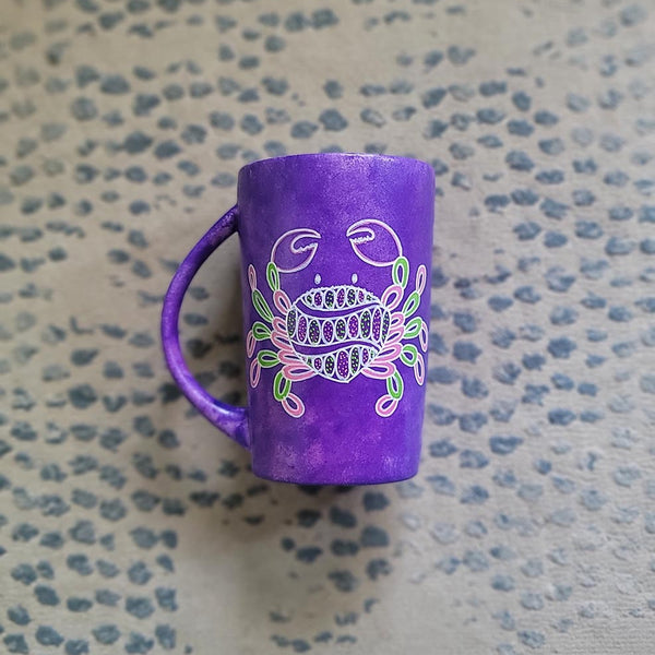 A hand-painted purple mug with cancer sign drawn on it