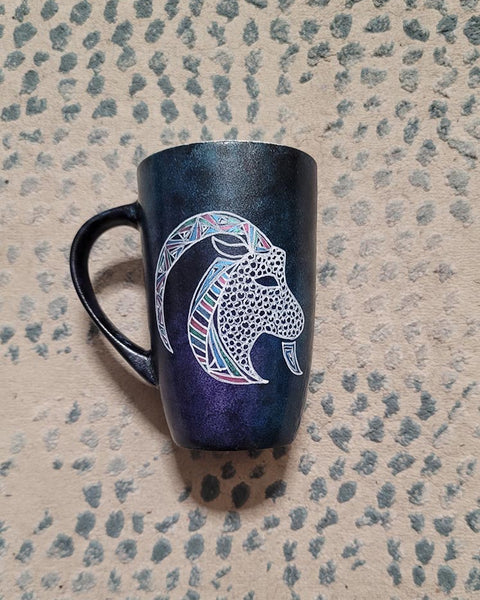 A Hand-painted dark galaxy mug with Capricorn sign in white and colored with patterns of pink blues and greens