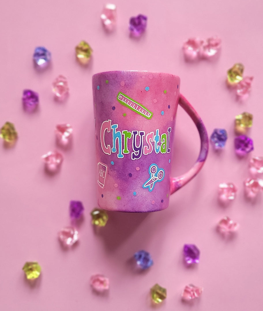 A Pink Hand painted Mug with the name "Chrystal" and school items scattered all over