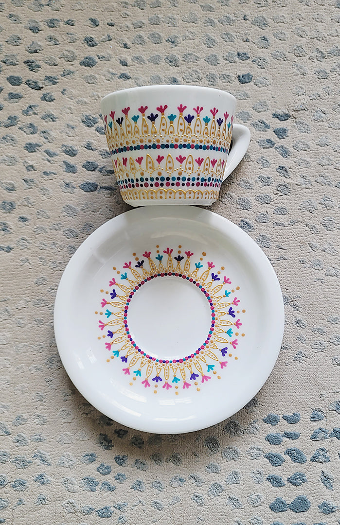 A White cup and saucer with patterns drawn in gold relief and small flowers in pinks, purples and turquoise