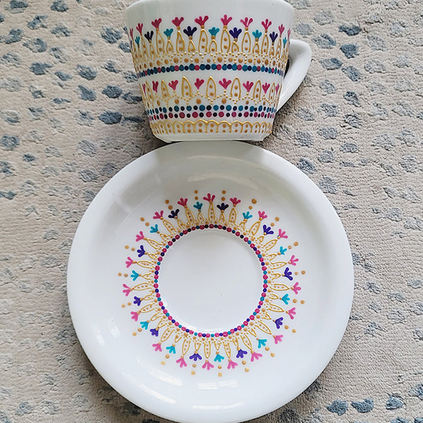 A White cup and saucer with patterns drawn in gold relief and small flowers in pinks, purples and turquoise