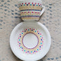 A White cup and saucer with patterns drawn in gold relief and small flowers in pinks, purples and turquoise