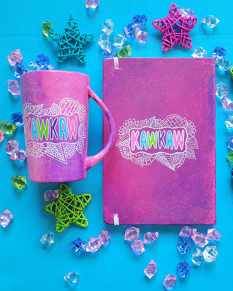 A pink galaxy hand painted mug and notebook with the name "kawkaw" inside a cloud of doodles