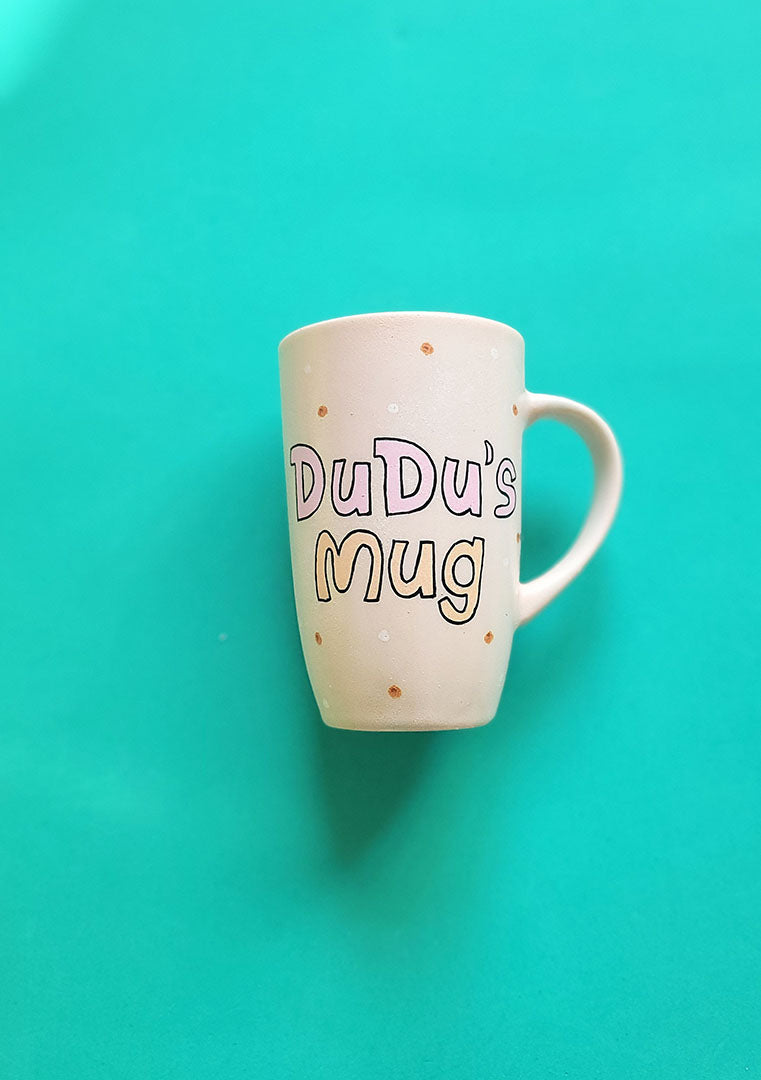 A Pale pink hand painted mug with the sentence "Dudu's Mug"