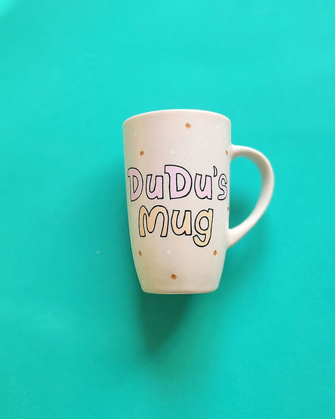 A Pale pink hand painted mug with the sentence "Dudu's Mug"