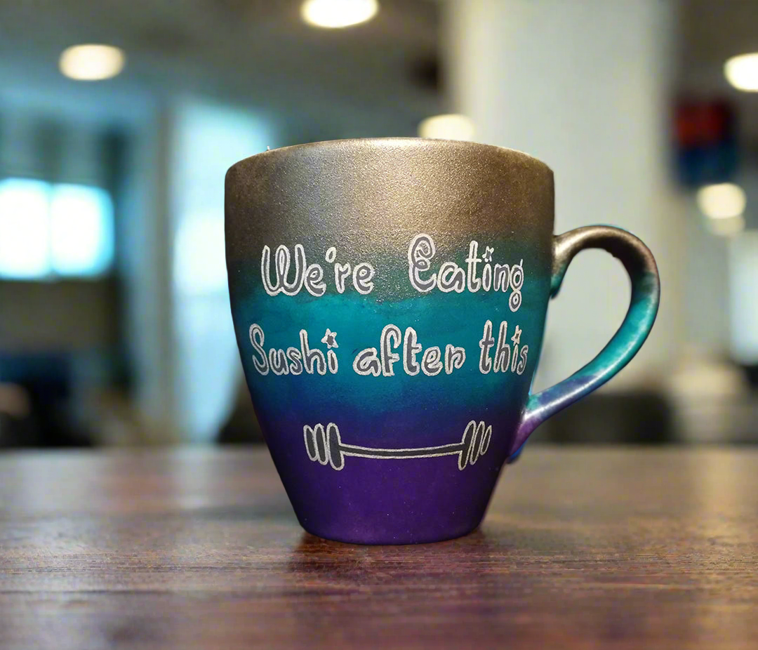 A gradient colored mug (Silver, turquoise and purple) with the words "we're eating sushi after this " and a small weight bar drawn below it