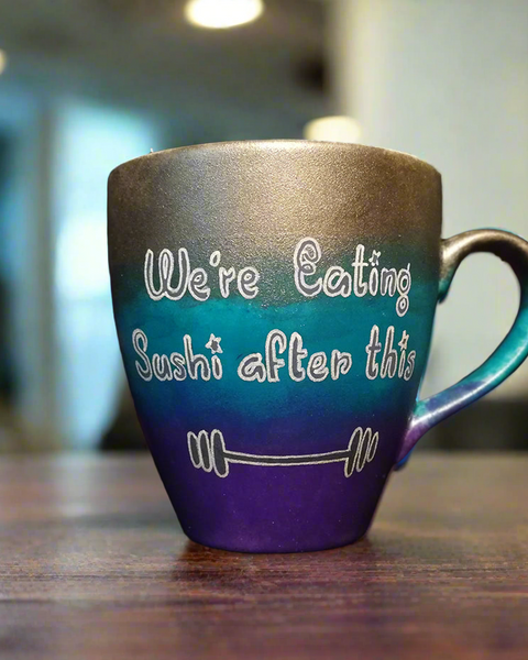 A gradient colored mug (Silver, turquoise and purple) with the words "we're eating sushi after this " and a small weight bar drawn below it