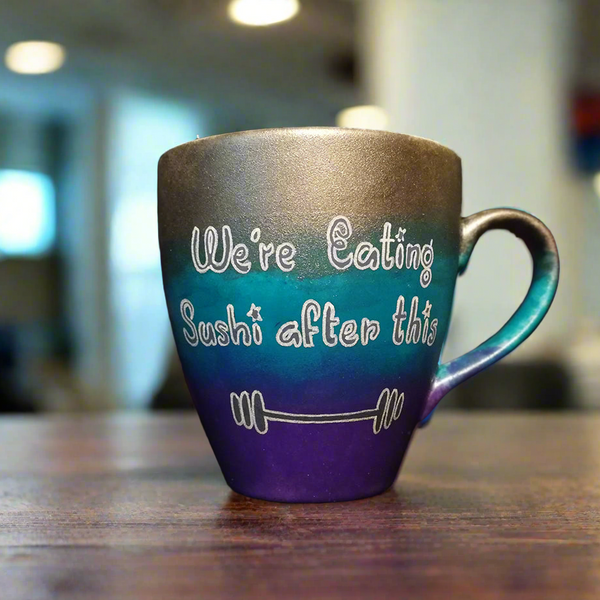 A gradient colored mug (Silver, turquoise and purple) with the words "we're eating sushi after this " and a small weight bar drawn below it