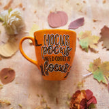 An orange hand painted mug with black dots scattered all over and the word 