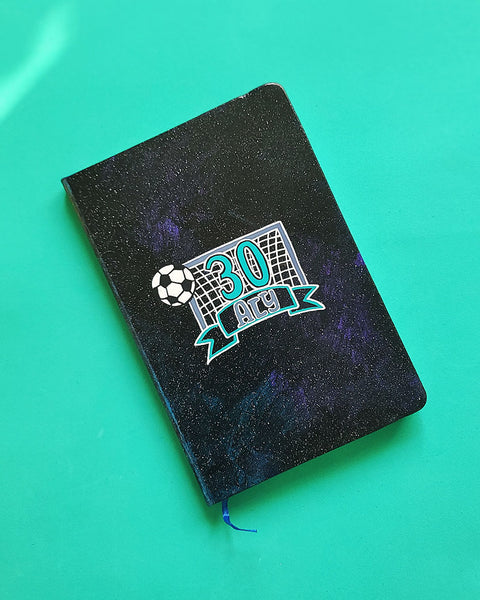 A Black Galaxy Hand Painted Notebook with the drawing of a football net and a football drawn at the corner . The number 30 written in the center of the net and under it the name Aly written