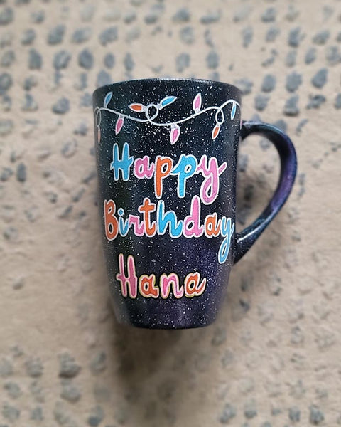 A Black Galaxy hand painted mug with lighting on the top and the words "happy birthday hana"