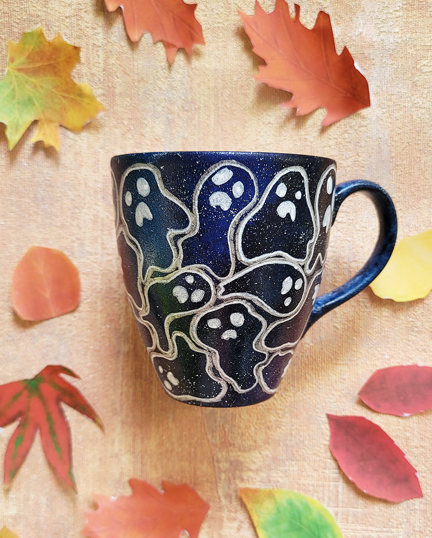 A Bluish Galaxy hand painted mug with ghosts painted all over in white and outlined with silver