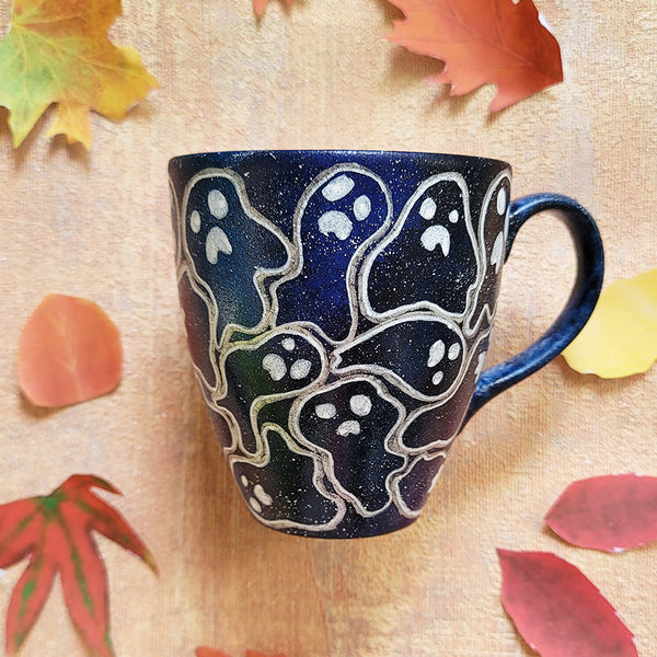 A Bluish Galaxy hand painted mug with ghosts painted all over in white and outlined with silver