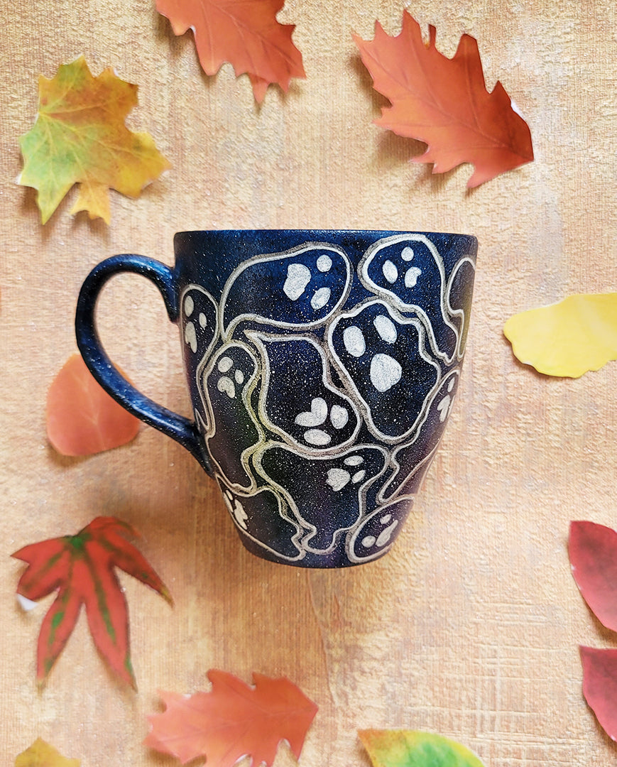 A Bluish Galaxy hand painted mug with ghosts painted all over in white and outlined with silver