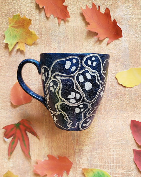 A Bluish Galaxy hand painted mug with ghosts painted all over in white and outlined with silver