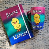 A Gift Set Hand painted in gradient colors (pink-green-blue) containing a mug and notebook with a duck painted in the center and the words Ashtar written above it and the word 