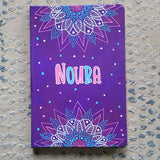 A Purple hand painted notebook with 2 half mandalas one on top and one at the bottom with the name 