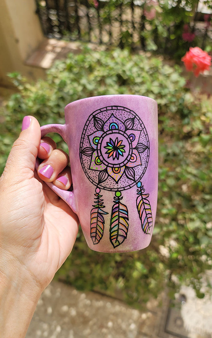 A Pastel Pink hand painted mug with a dreamcatcher in black and colored in with (pink, yellow, purple blue, green and orange)