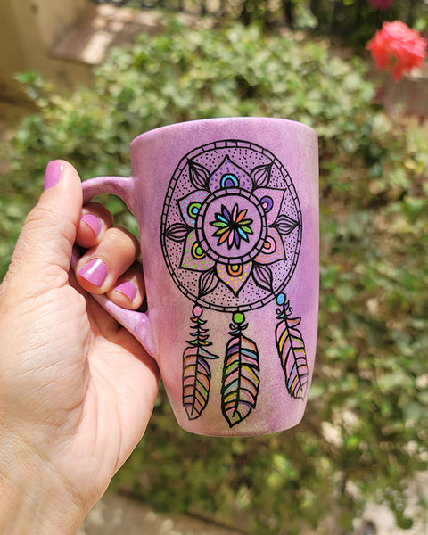 A Pastel Pink hand painted mug with a dreamcatcher in black and colored in with (pink, yellow, purple blue, green and orange)